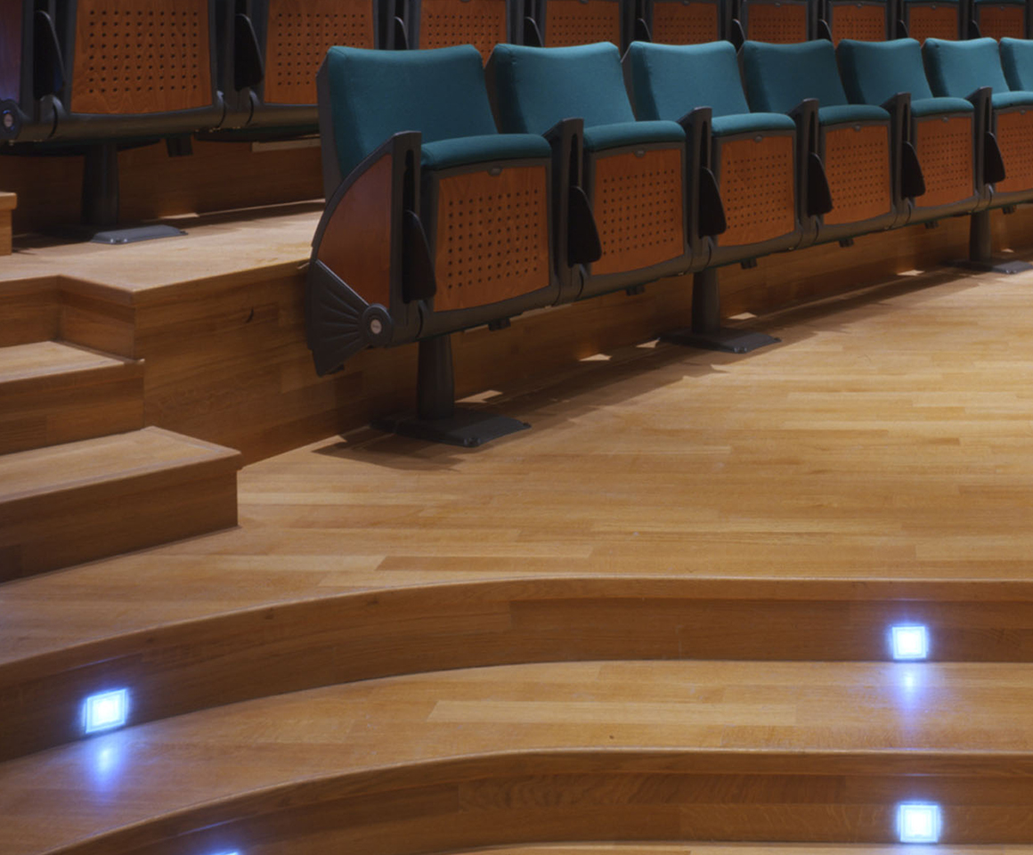 Dettaglio pavimento e gradini in parquet con poltroncine per il pubblico.