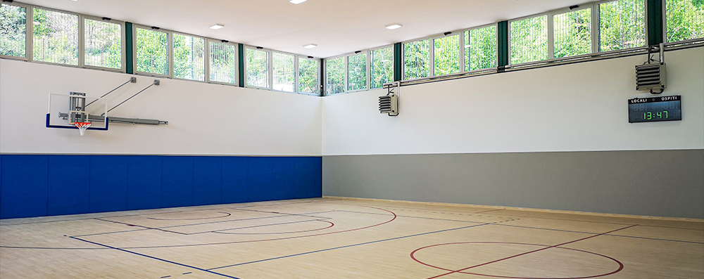 Interno palestra con pavimento in parquet sportivo e rivestimenti murali, attrezzature giochi sportivi.