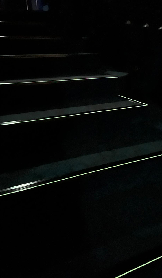 Dettaglio profili fotoluminescenti installati sui gradini e pavimento in moquette di una sala cinematografica e per conferenze.